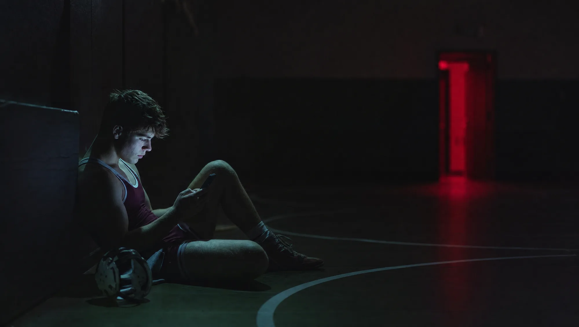 A wrestler alone in a dark room reviewing match footage on a phone